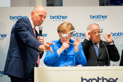 Bild mit Symbolcharakter: Auf der diesjährigen CeBIT erklärt Matthias Kohlstrung, Geschäftsführer von Brother Deutschland, Kanzlerin Angela Merkel die Augmented-Reality-Brille “AirScouter” seines Unternehmens – doch die Kanzlerin ist noch etwas ratlos, was sich mit der neuen Technologie anfangen lässt. (Bild: Bundesregierung/Güngör) Bild mit Symbolcharakter: Auf der diesjährigen CeBIT erklärt Matthias Kohlstrung, Geschäftsführer von Brother Deutschland, Kanzlerin Angela Merkel die Augmented-Reality-Brille “AirScouter” seines Unternehmens – doch die Kanzlerin ist noch etwas ratlos, was sich mit der neuen Technologie anfangen lässt. (Bild: Bundesregierung/Güngör)