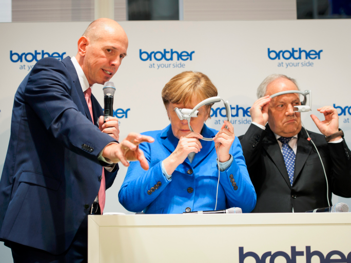 Bild mit Symbolcharakter: Auf der diesjährigen CeBIT erklärt Matthias Kohlstrung, Geschäftsführer von Brother Deutschland, Kanzlerin Angela Merkel die Augmented-Reality-Brille “AirScouter” seines Unternehmens – doch die Kanzlerin ist noch etwas ratlos, was sich mit der neuen Technologie anfangen lässt. (Bild: Bundesregierung/Güngör)